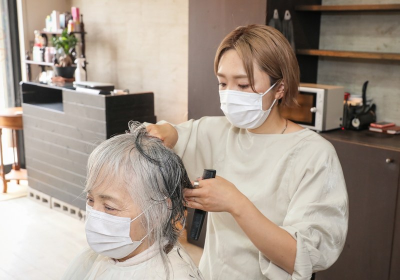 マスクを着けたスタイリストがお客様のウィッグをカットする様子